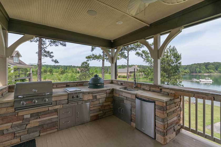 An outdoor kitchen with slates and grill along the lake side with a view of forests in front.