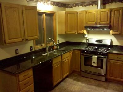 A medium-sized kitchen with used granite countertop space and wooden cabinets mounted on the wall.