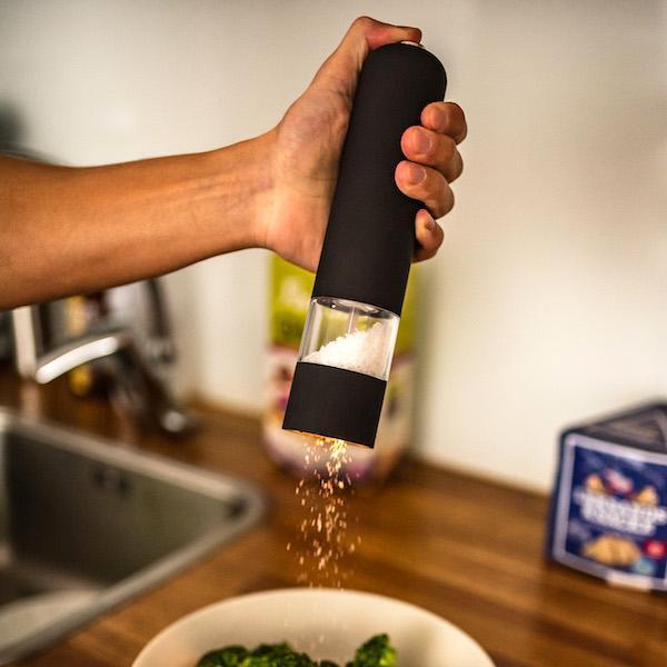 A black colored spice grinder in the hand of a person grinding spice, a useful small kitchen appliance.