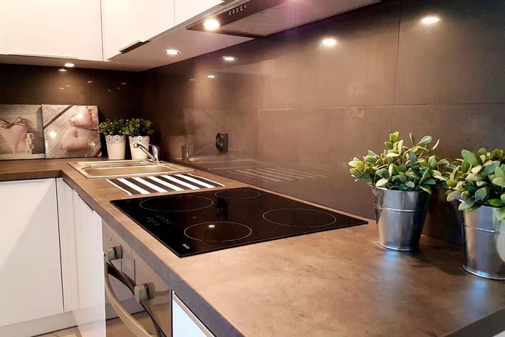 Brownish finish kitchen with an automatic stove in the center of the main shelf. Stainless steel sink and flower pots are also installed. 