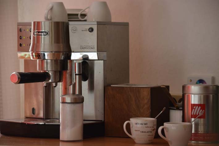 An electric coffee maker made of steel placed on a wooden countertop is a small kitchen appliance.