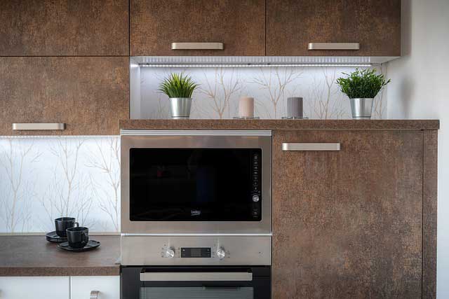 Elegant silver microwave oven with brown cabinets and green plant pots on top.