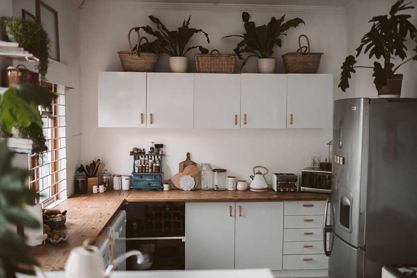 White kitchen cabinets with brown countertop and grey fridge on the side